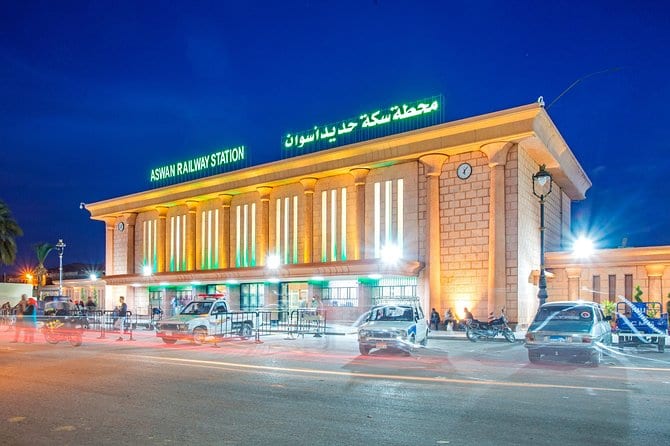 Aswan Railway Station lit up at night, with its name in English and Arabic above the colonnaded entrance