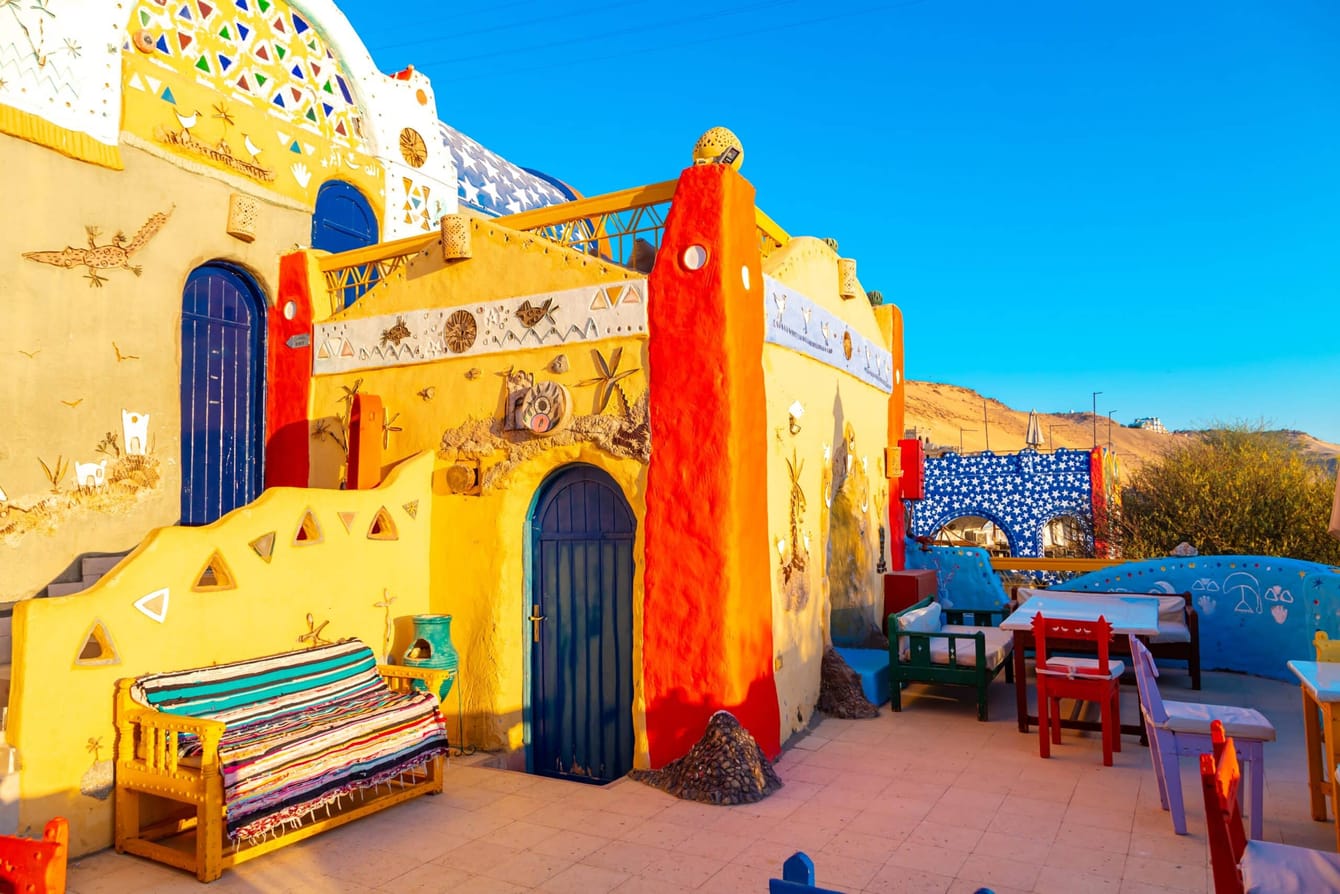 A Nubian village house on the west bank at Aswan, painted in yellow, orange and blue with patterned decoration around the door, and a terrace set with tables